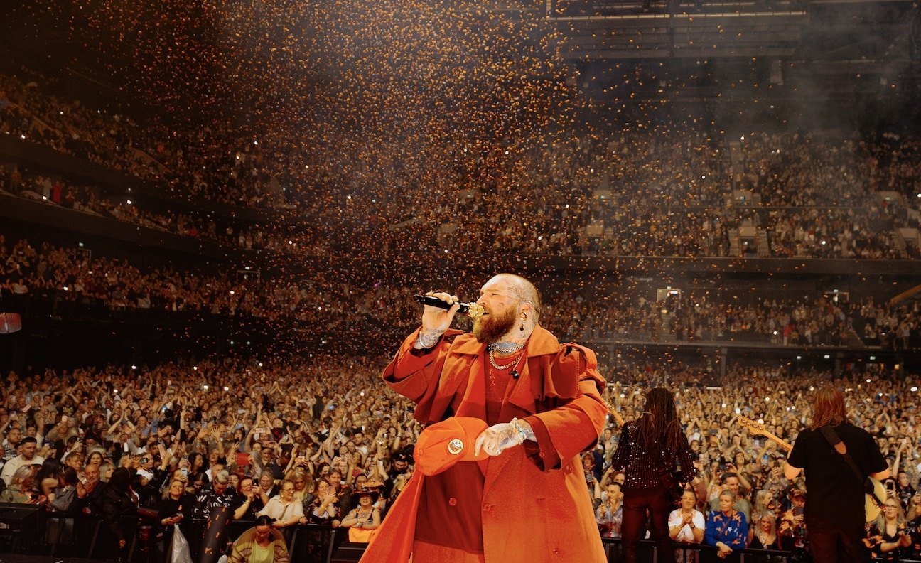 A performer in an orange coat singing to a full arena as golden confetti falls